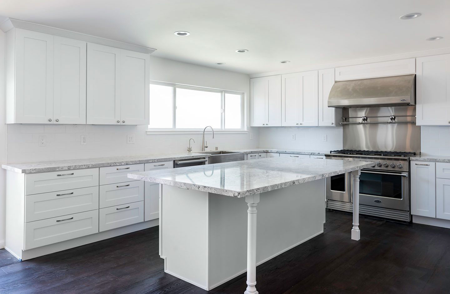 A modern kitchen with white cabinets, stainless steel appliances, a large island with a marble countertop, and a sleek design.