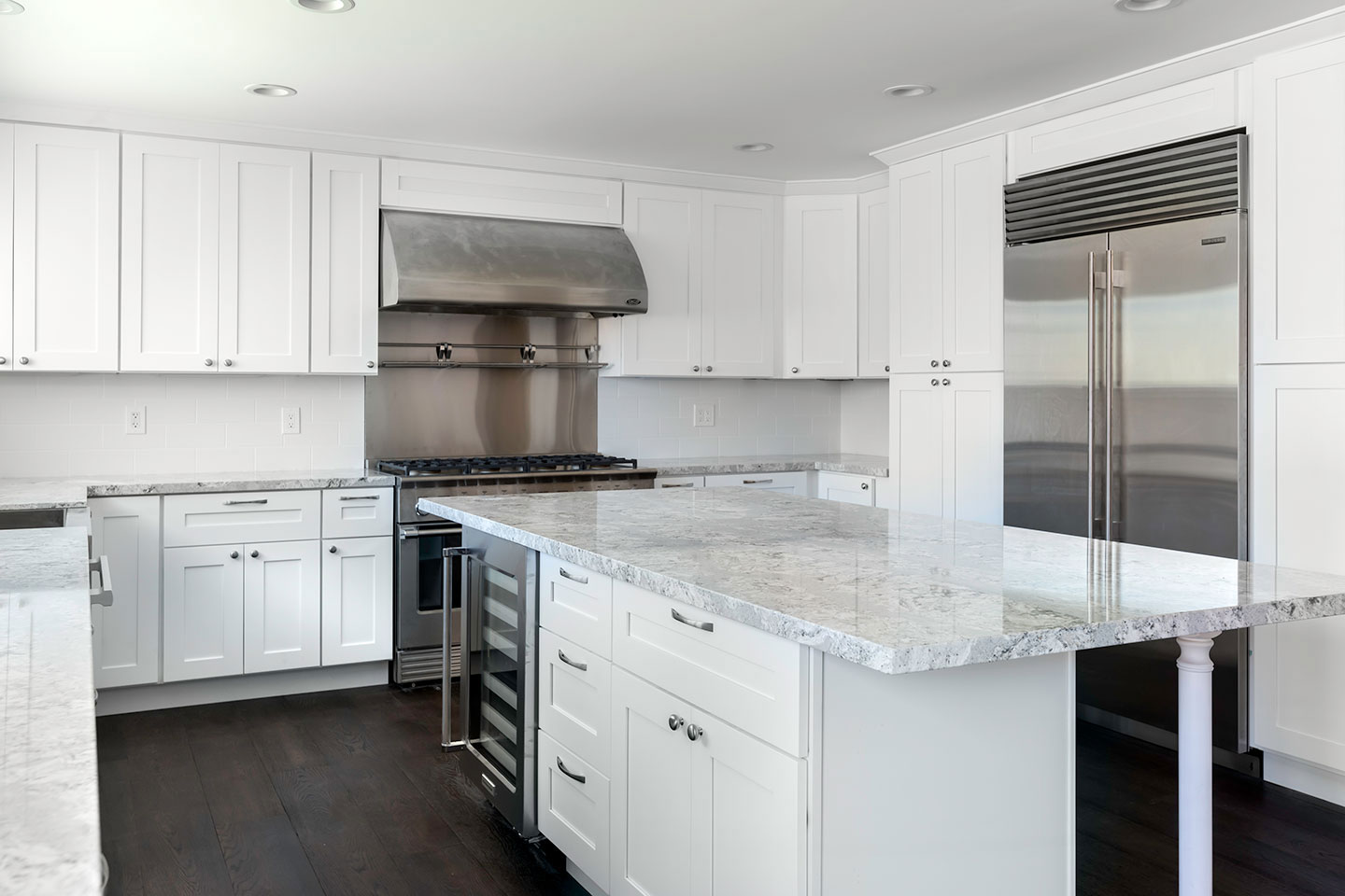 A modern kitchen with white cabinets, marble countertops, stainless steel appliances, and a center island.