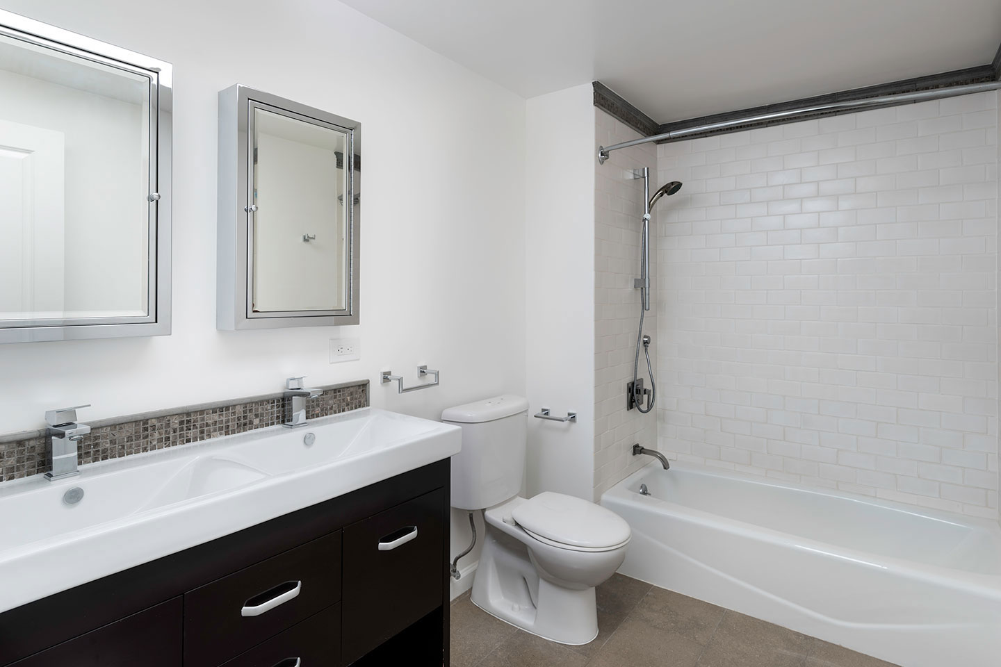 The image shows a modern bathroom with a white toilet, sink, and bathtub, featuring black countertops, white tiles, and a large mirror above the sink.