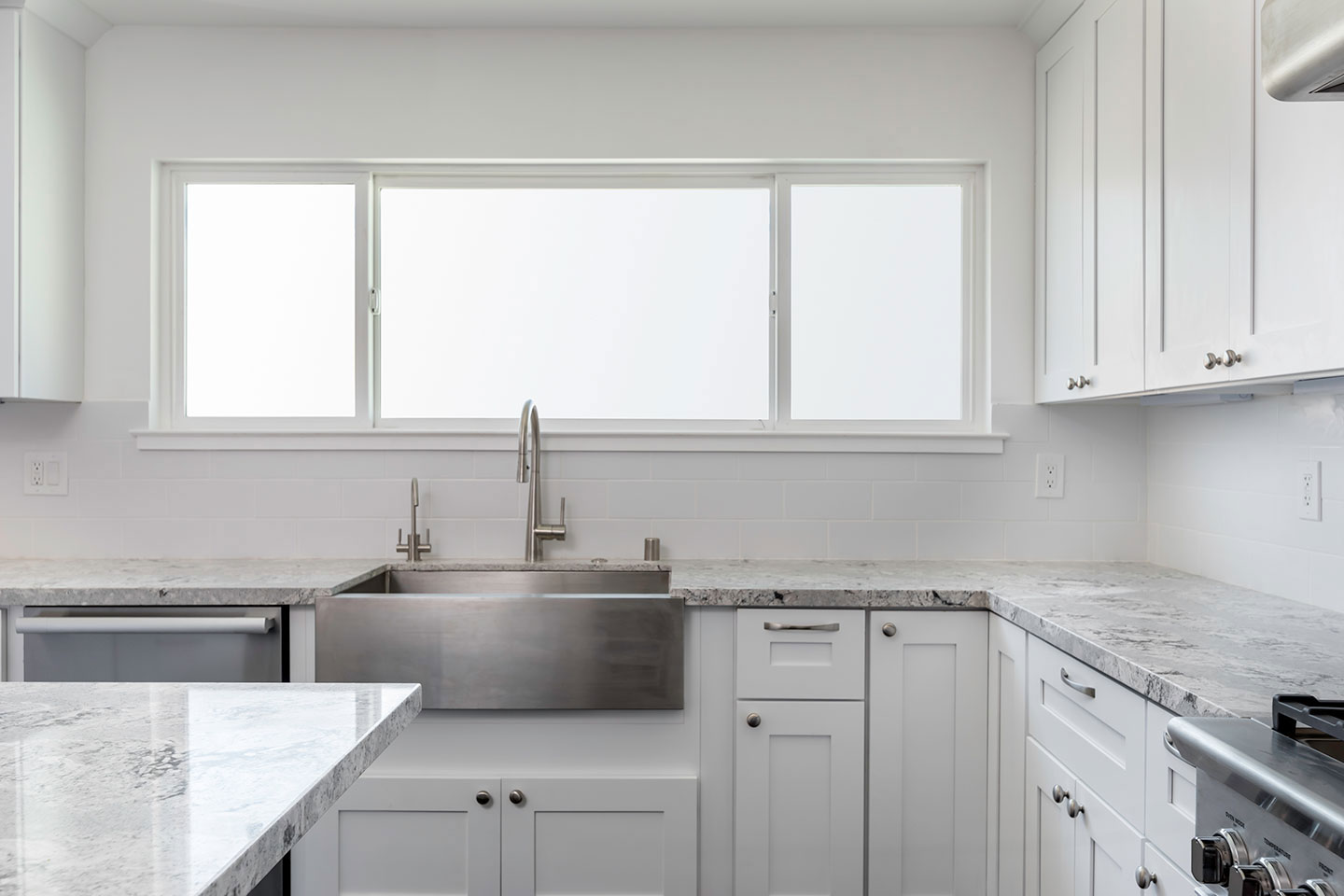 The image shows a modern kitchen with white cabinets, granite countertops, stainless steel appliances, a sink, and a window allowing natural light into the space.