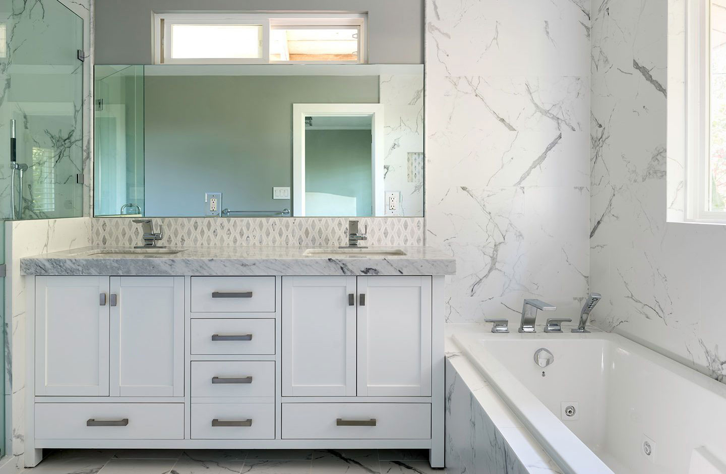 A modern bathroom with marble countertops, white cabinetry, a large mirror above the sink, and a clean, minimalist design.