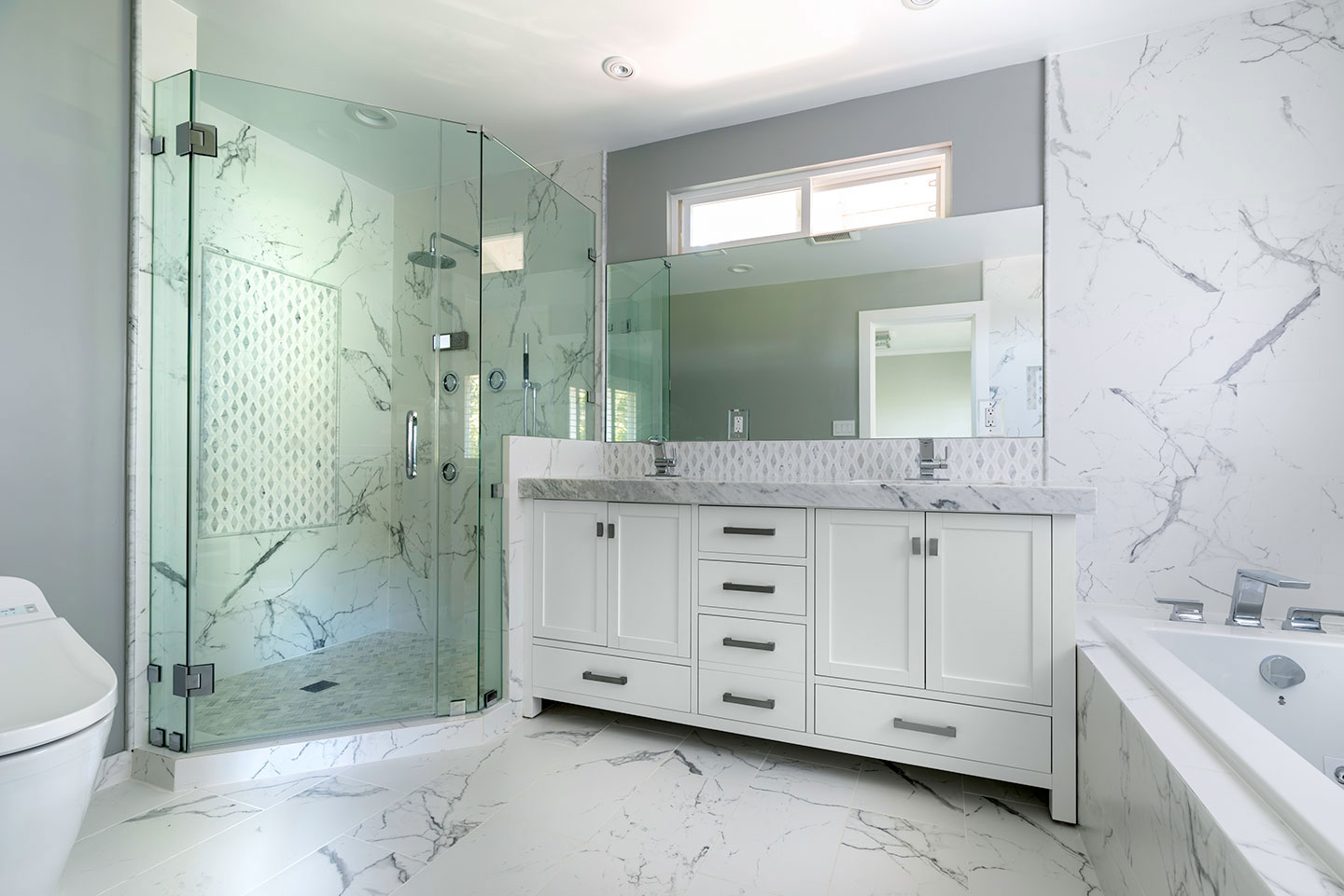 The image shows a modern bathroom with marble-patterned walls, a large glass shower enclosure, a white vanity with cabinets, a stainless steel sink, and a toilet.