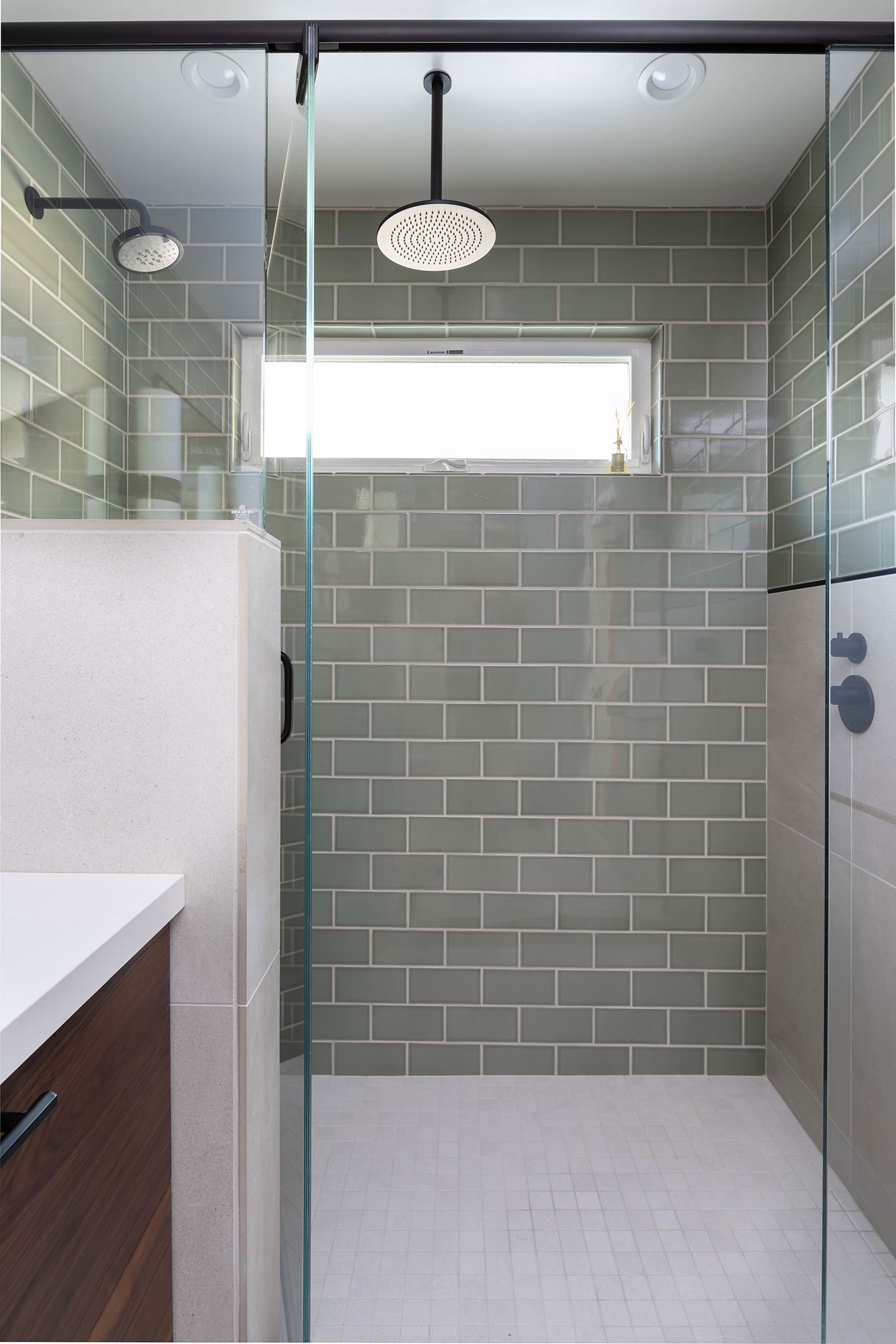 The image shows a modern bathroom interior with a glass-enclosed shower stall featuring green subway tiles, a white towel rack, and a frosted glass door.