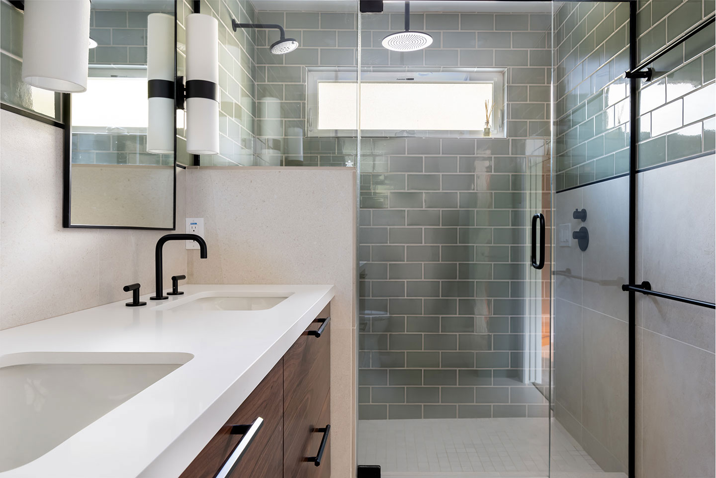 The image shows a modern bathroom with a green tiled wall, white countertops, a glass shower door, and a brown vanity cabinet.