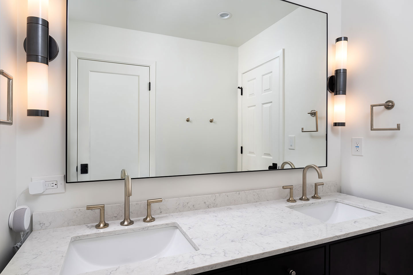 A modern bathroom with a marble countertop, double sinks, gold fixtures, and a large mirror reflecting the room s interior.