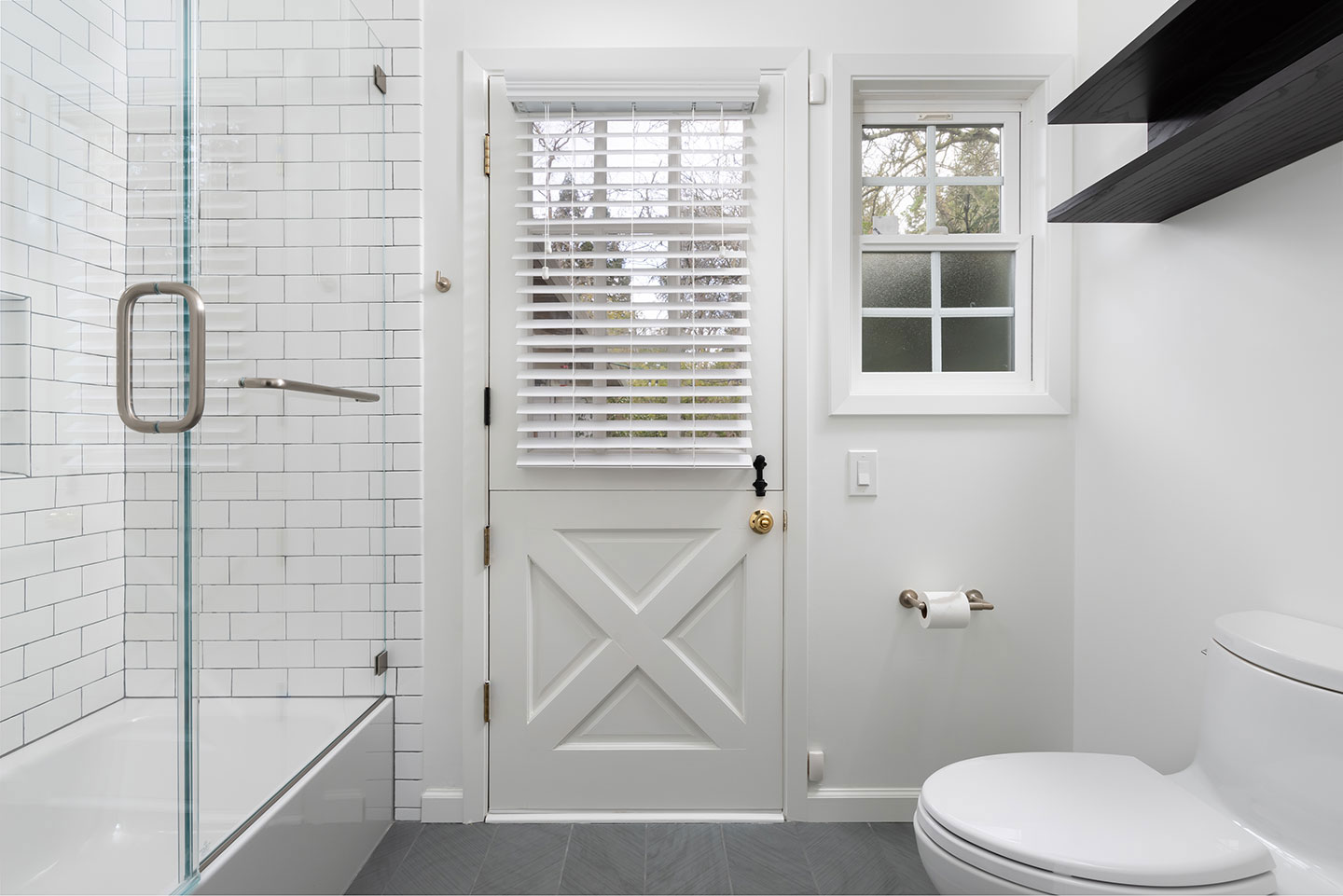 The image shows a modern bathroom interior with a white color scheme, featuring a glass shower door, a white sink, a toilet, a dark wooden door, and tiled walls.