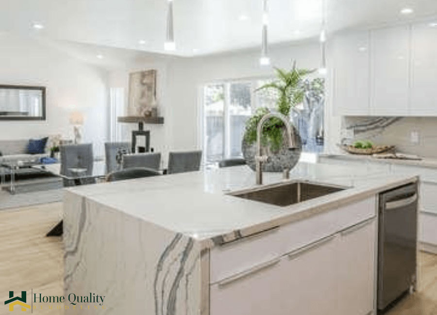 The image displays a modern kitchen interior with contemporary design elements such as sleek countertops, stainless steel appliances, a large island with a sink, and a clean, minimalist aesthetic.