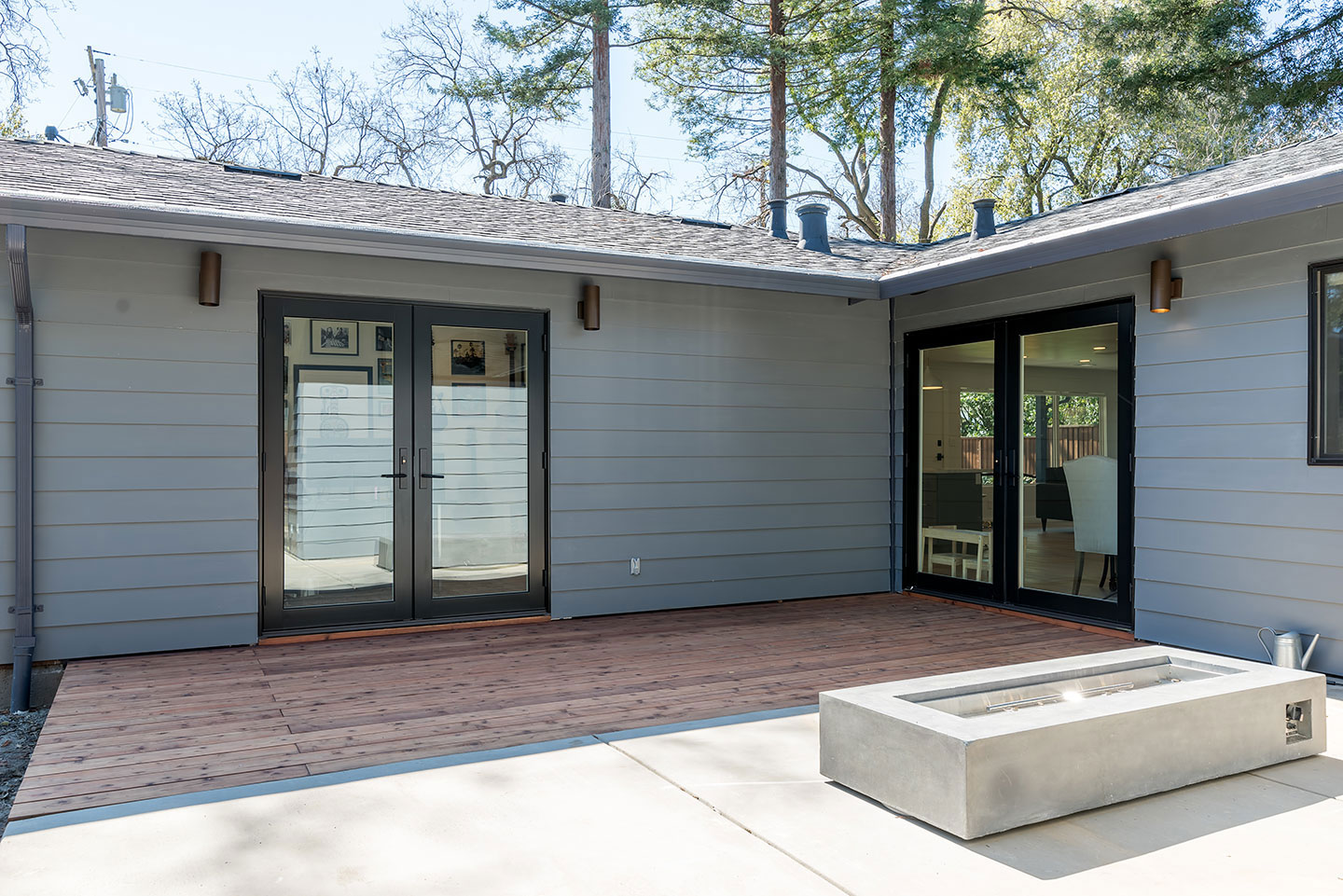 A modern single-story house with a covered patio featuring a large sliding glass door, leading to an outdoor seating area with a fireplace and a hot tub, set against a clear sky.