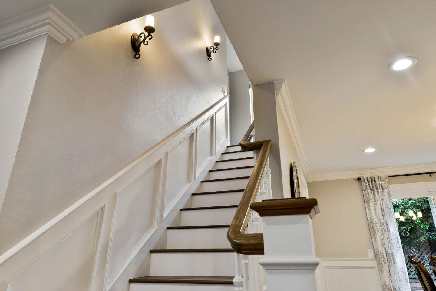 The image shows an interior staircase with white railings leading up to a landing, featuring a wooden floor and a wall-mounted light fixture above the stairs.