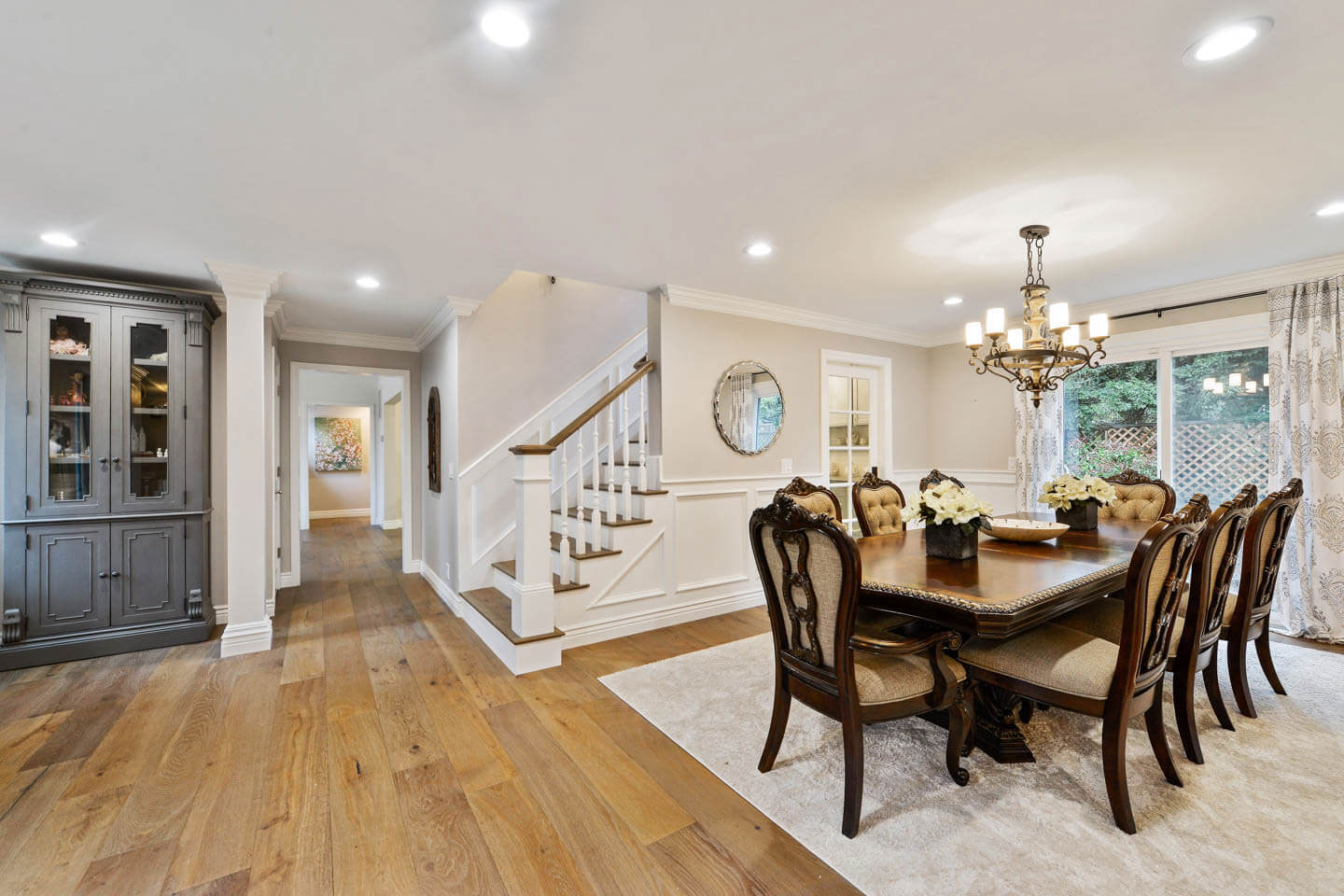This is a photograph of an interior space showcasing a modern kitchen with hardwood floors, a center island, and contemporary cabinetry, leading to a dining area with a wooden table and chairs.