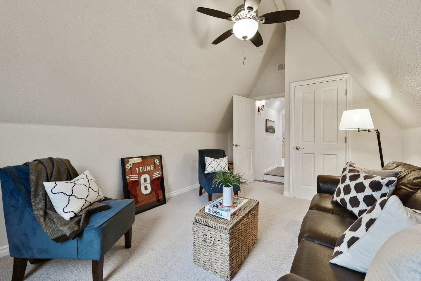 The image depicts a neatly arranged living room with a sloped ceiling, furniture, and decorations.