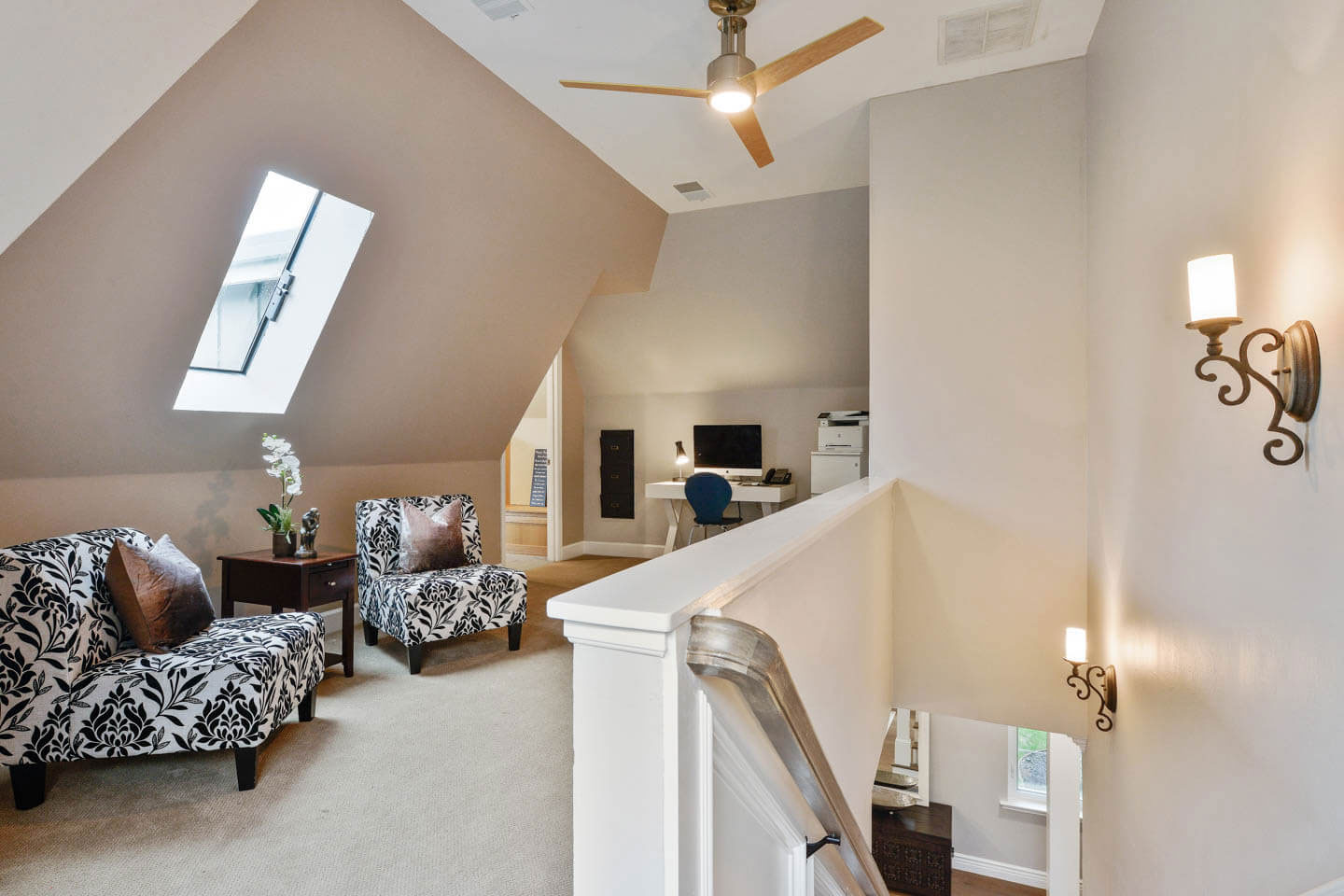 The image depicts an interior space with a modern design featuring a high ceiling, vaulted living room area, white walls, a dark wooden floor, a large skylight, recessed lighting, a staircase with a metal railing, and contemporary furniture including a sofa, armchairs, and a coffee table.