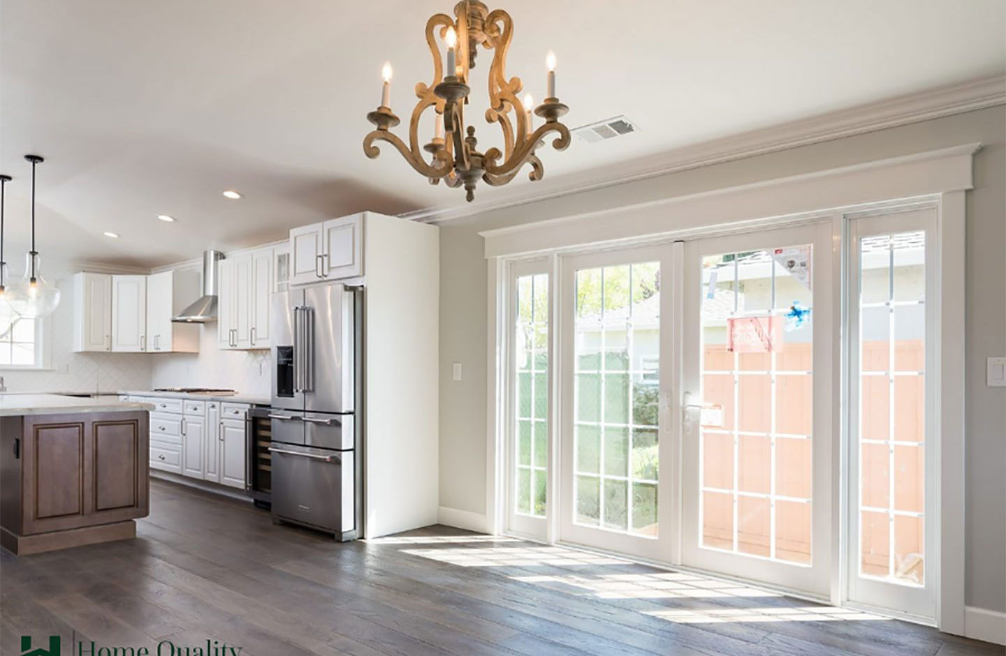 A brightly lit kitchen with white cabinets, stainless steel appliances, and large windows allowing natural light to flood the room.