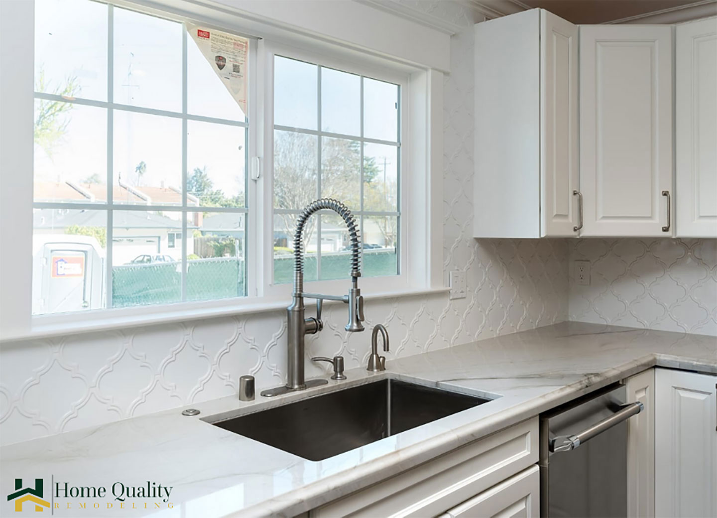 The image shows a modern kitchen interior with white cabinets, a stainless steel sink faucet, a black countertop, and a clean, well-lit space.