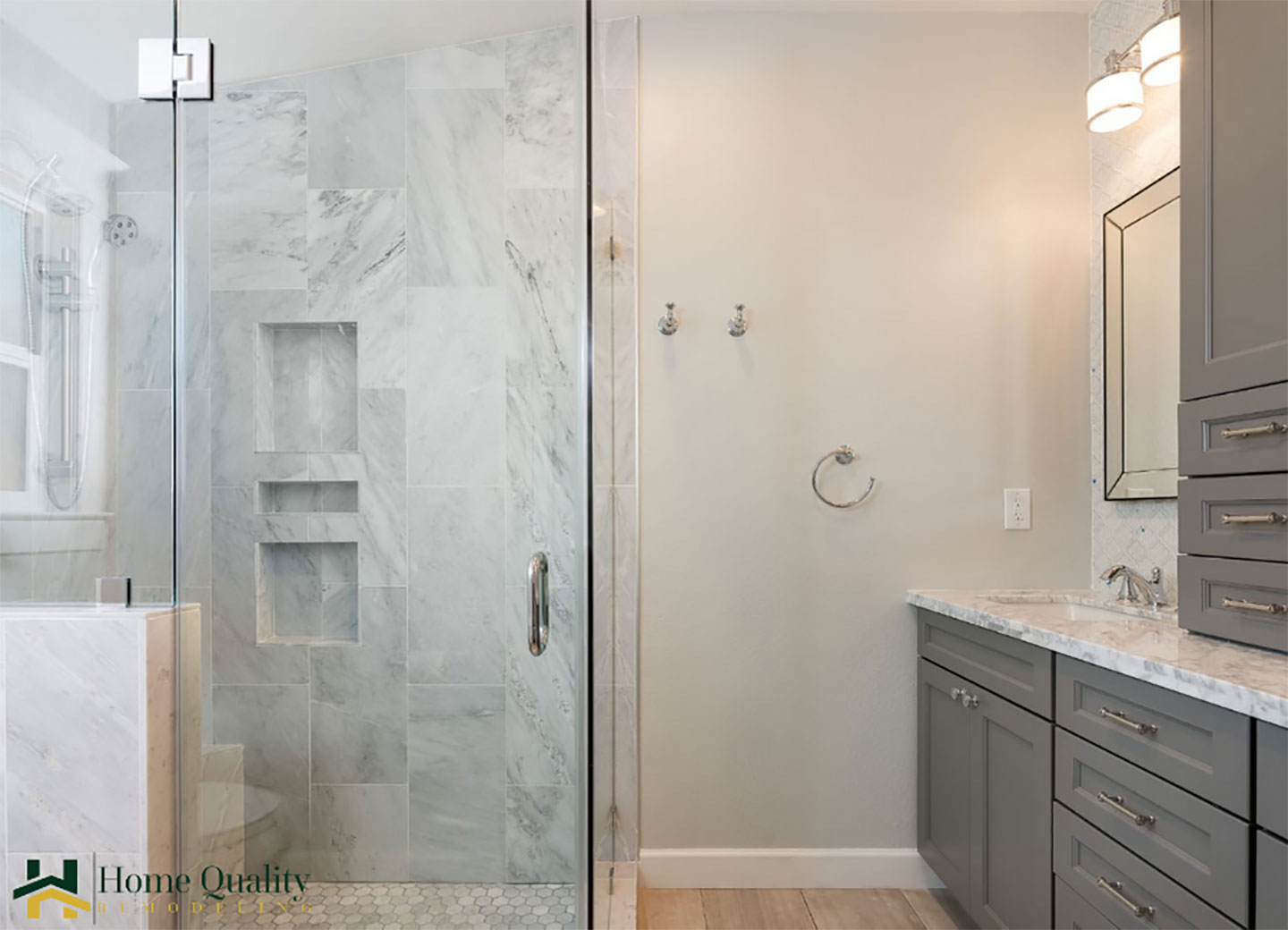 The image shows a modern bathroom interior with a large glass-enclosed shower stall featuring marble tiles, a walk-in shower, and a sleek design.