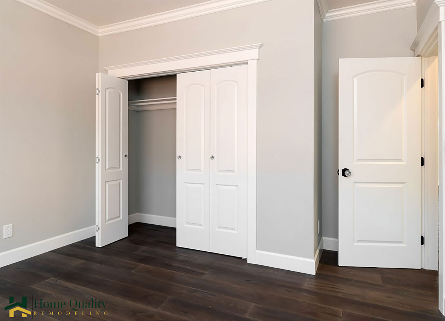 The image shows an interior view of a room with open doors leading to two separate rooms, possibly bedrooms or closets, with visible closet interiors and white walls, presented in a real estate context with a watermark or logo at the bottom right corner.