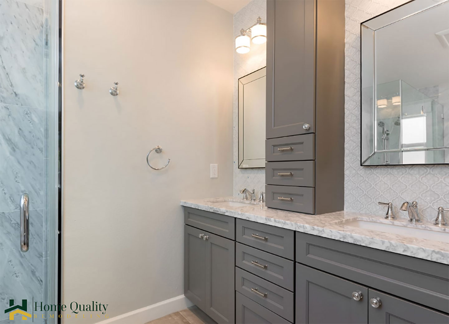 The image shows a modern bathroom interior with a gray cabinet, marble countertops, a large mirror, and a walk-in shower.