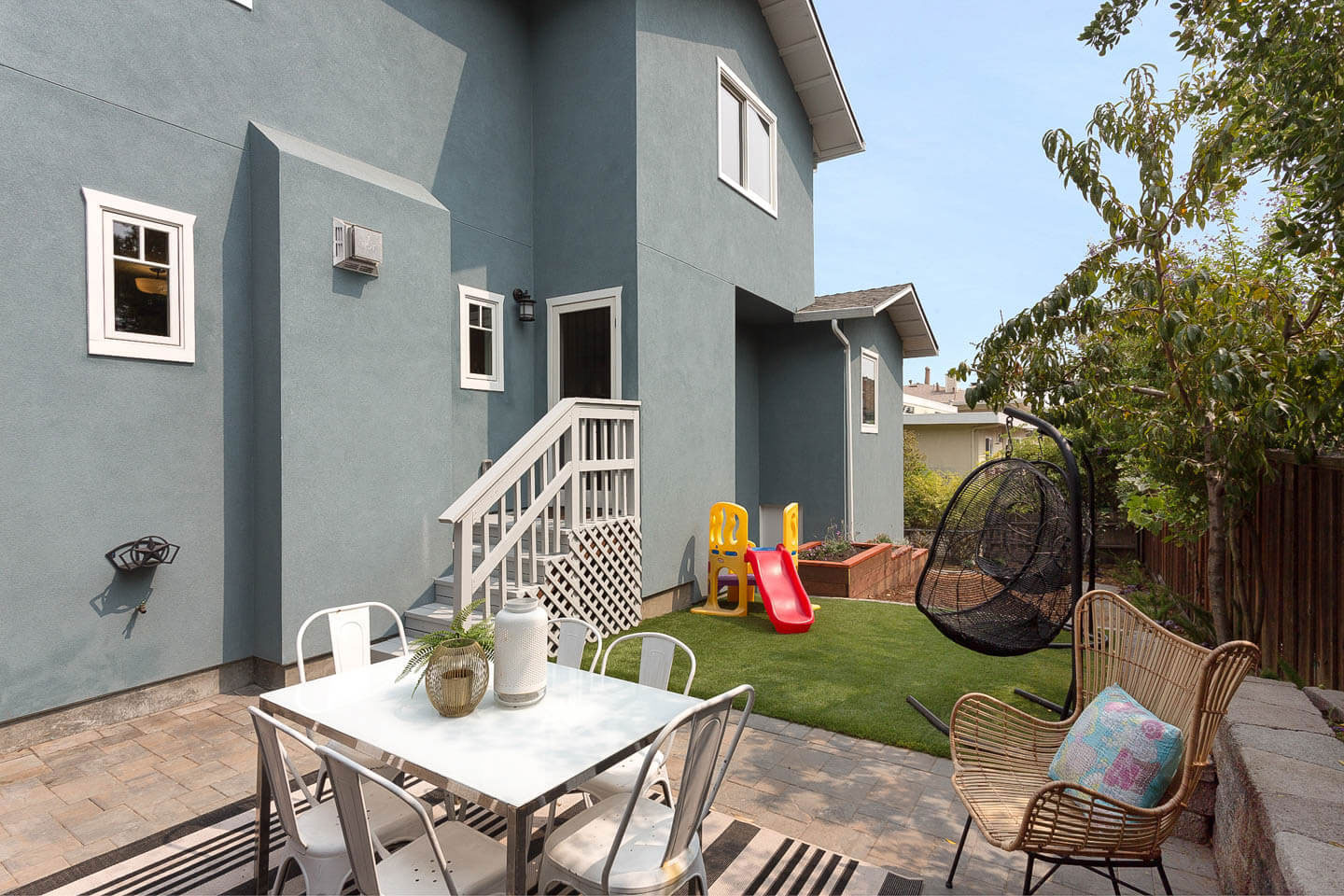 A modern two-story house with a backyard patio area featuring outdoor furniture, a playground, and a well-maintained lawn.
