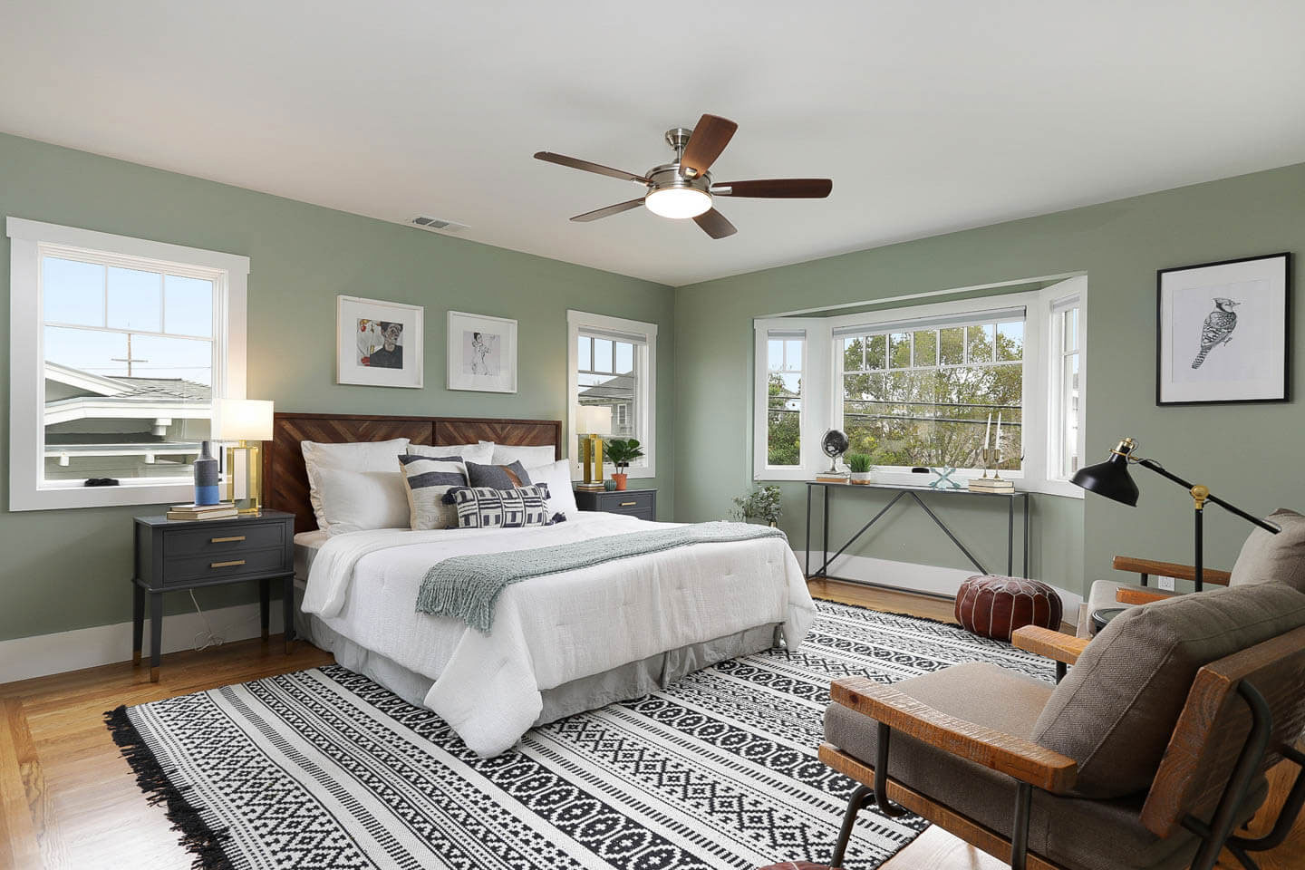 The image depicts a tastefully decorated bedroom with a large rug featuring a geometric pattern, a bed with a white comforter, a nightstand, a dresser, and a window with a view of the outdoors.
