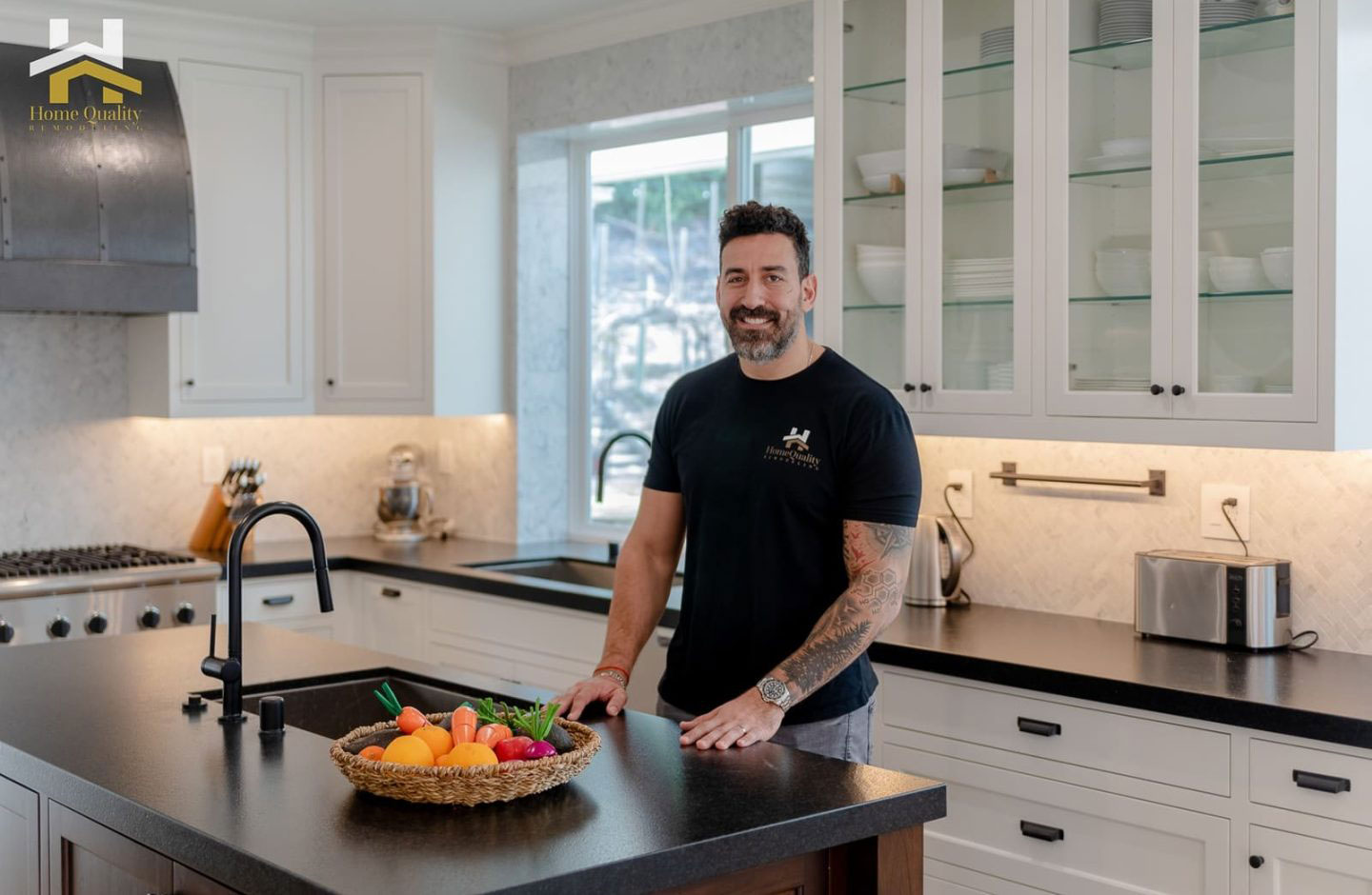 A man stands at a kitchen counter with a bowl of fruit, smiling towards the camera.