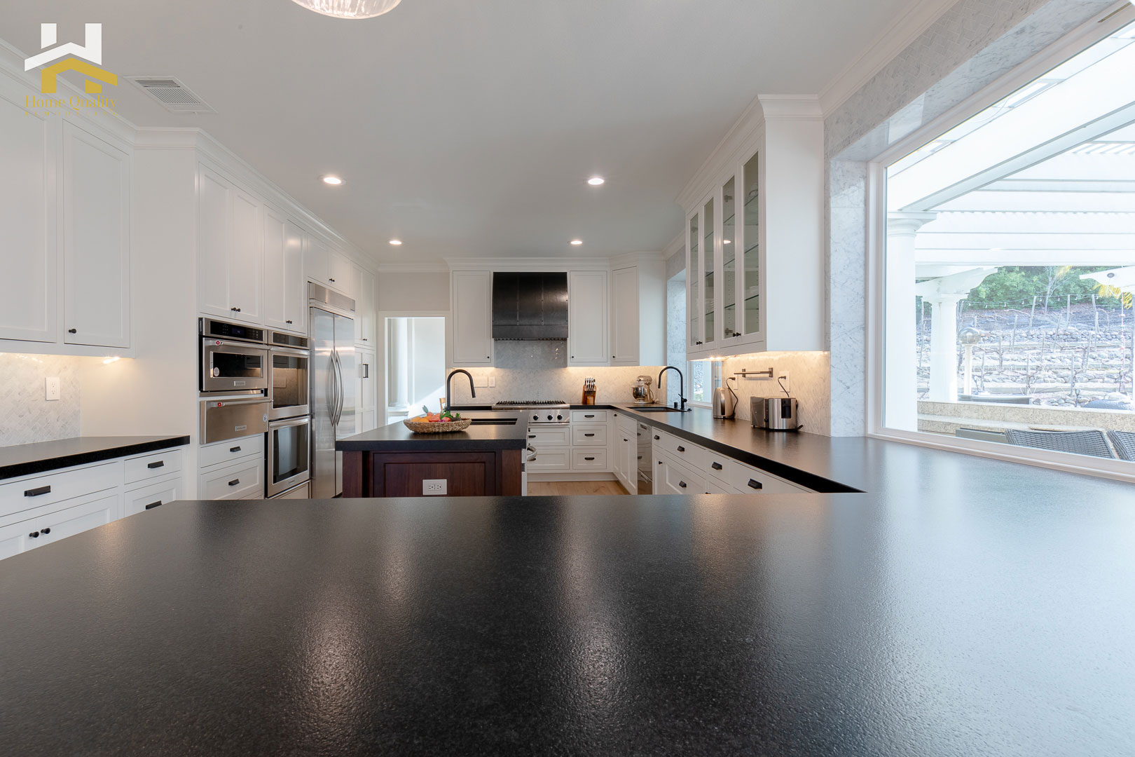 A modern kitchen interior with black countertops, white cabinets, stainless steel appliances, and a large island in the center.