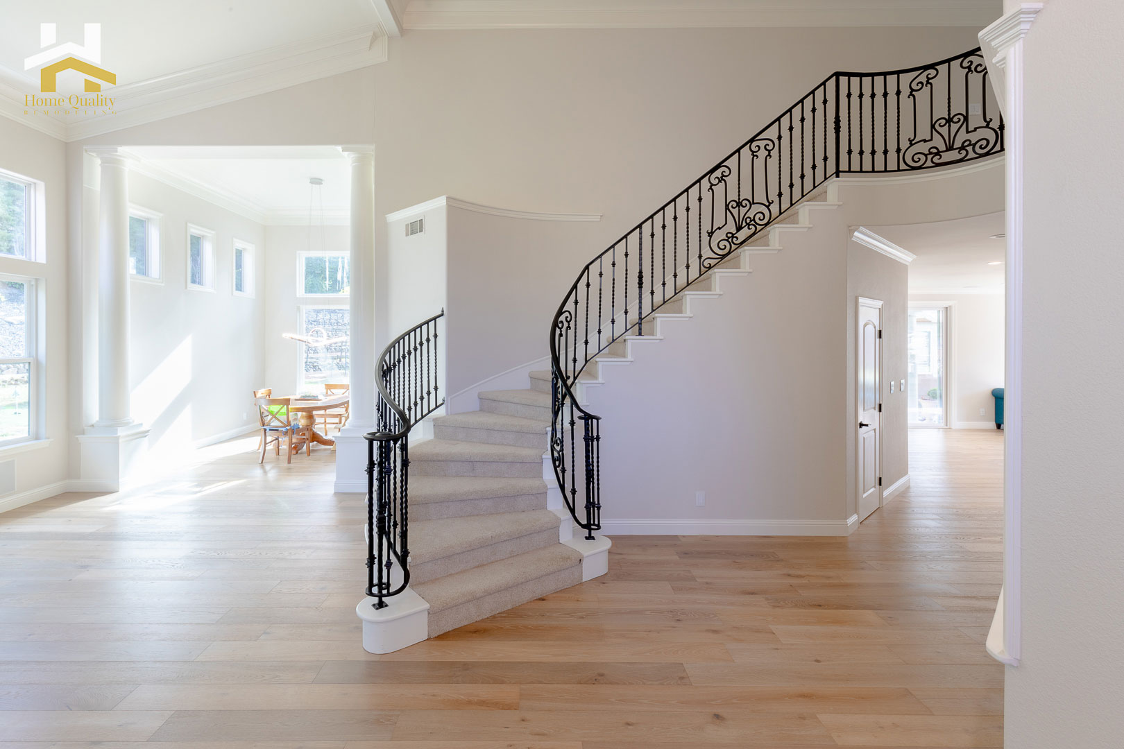 The image shows a spacious, well-lit interior hallway with white walls, hardwood floors, a staircase with a metal railing leading to an upper level, and a modern design aesthetic.