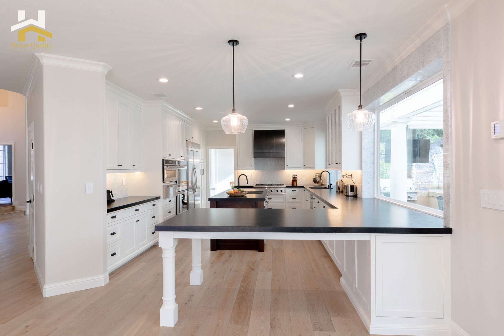 A modern kitchen with a central island, white cabinets, black countertops, and stainless steel appliances.