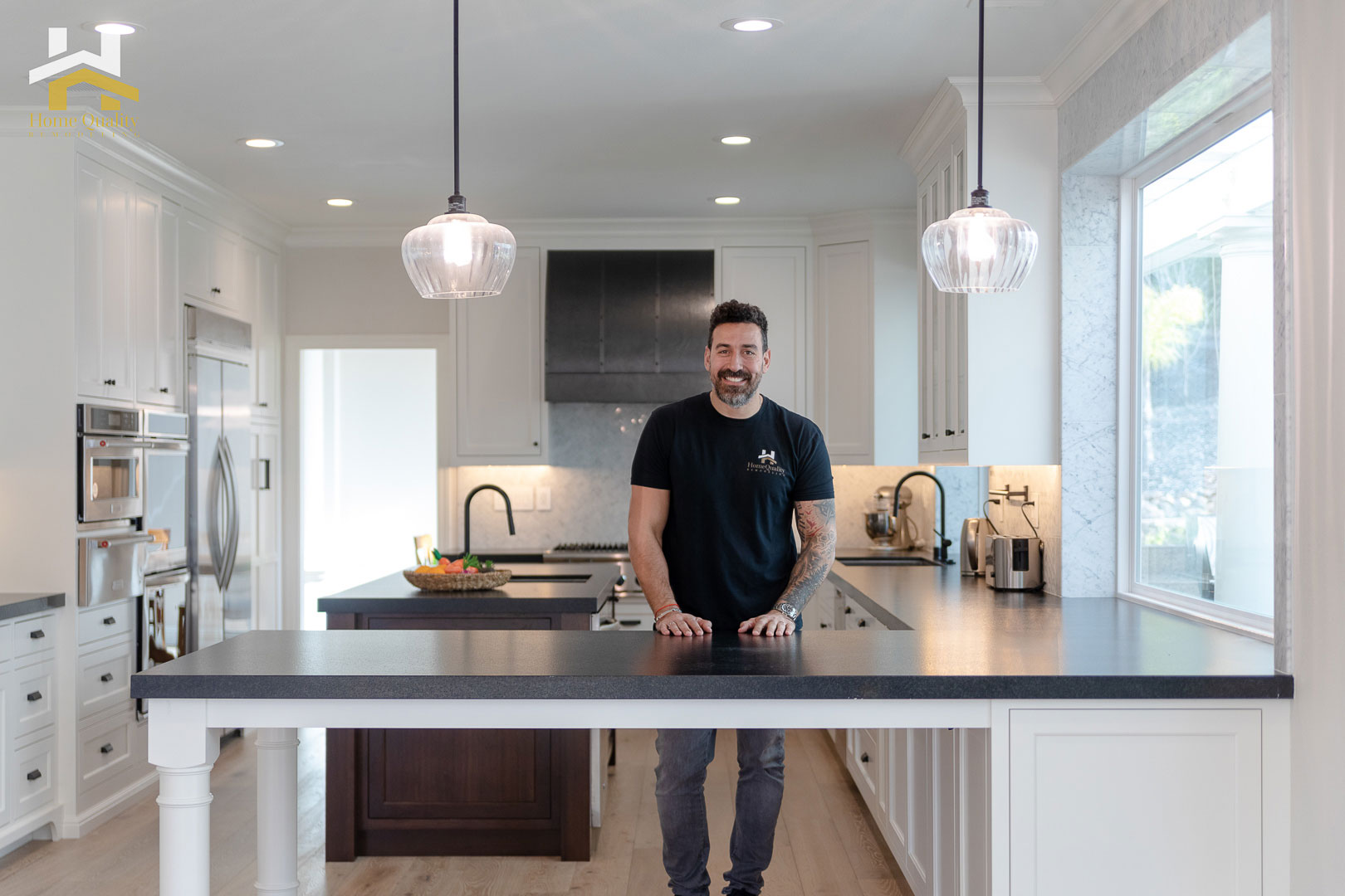A man stands at a kitchen island with a modern design featuring granite countertops, stainless steel appliances, and a black and white color scheme.