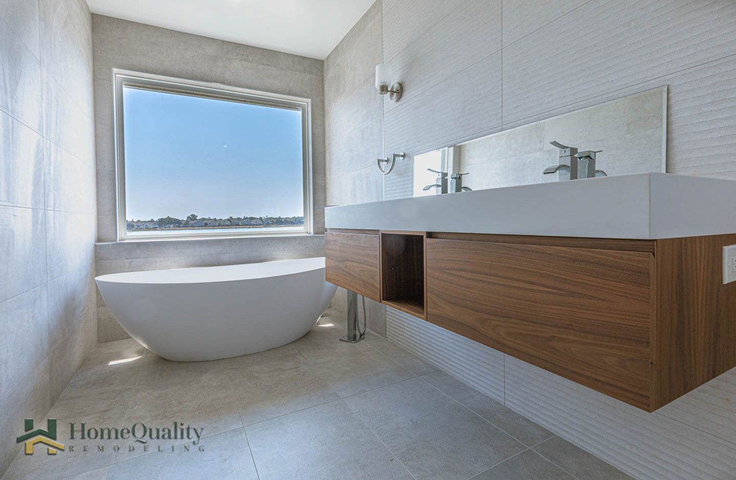 The image shows a modern bathroom with a white bathtub, a large mirror above the sink, wooden cabinets, a white countertop, and a wooden bench.