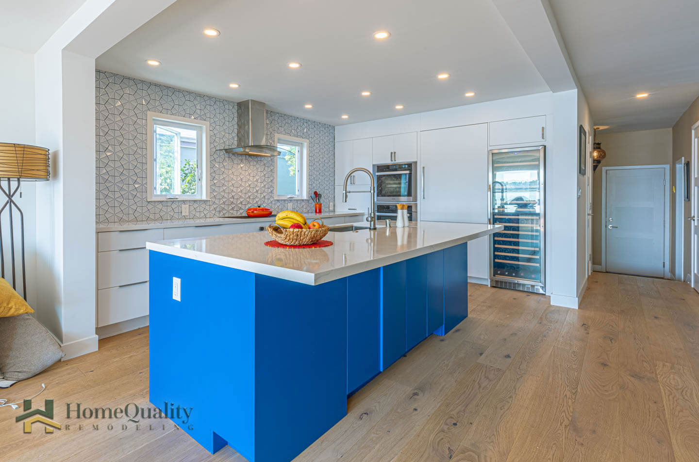A modern kitchen with blue cabinets, white countertops, stainless steel appliances, and hardwood flooring.