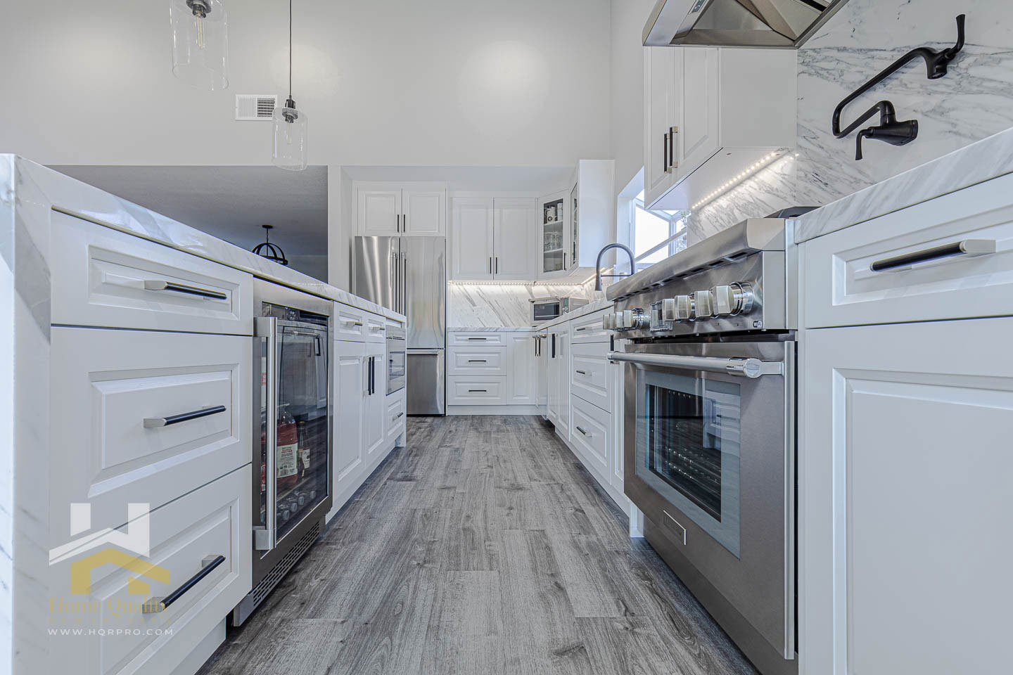 The image shows a modern kitchen interior with white cabinetry, stainless steel appliances, and a large island in the center.