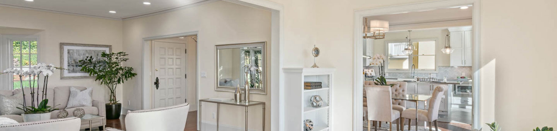 The image depicts a spacious room with a modern kitchen area on the right, featuring white cabinets and stainless steel appliances, and an open plan living space with light-colored walls and flooring, furnished with contemporary furniture, including a sofa and a coffee table.