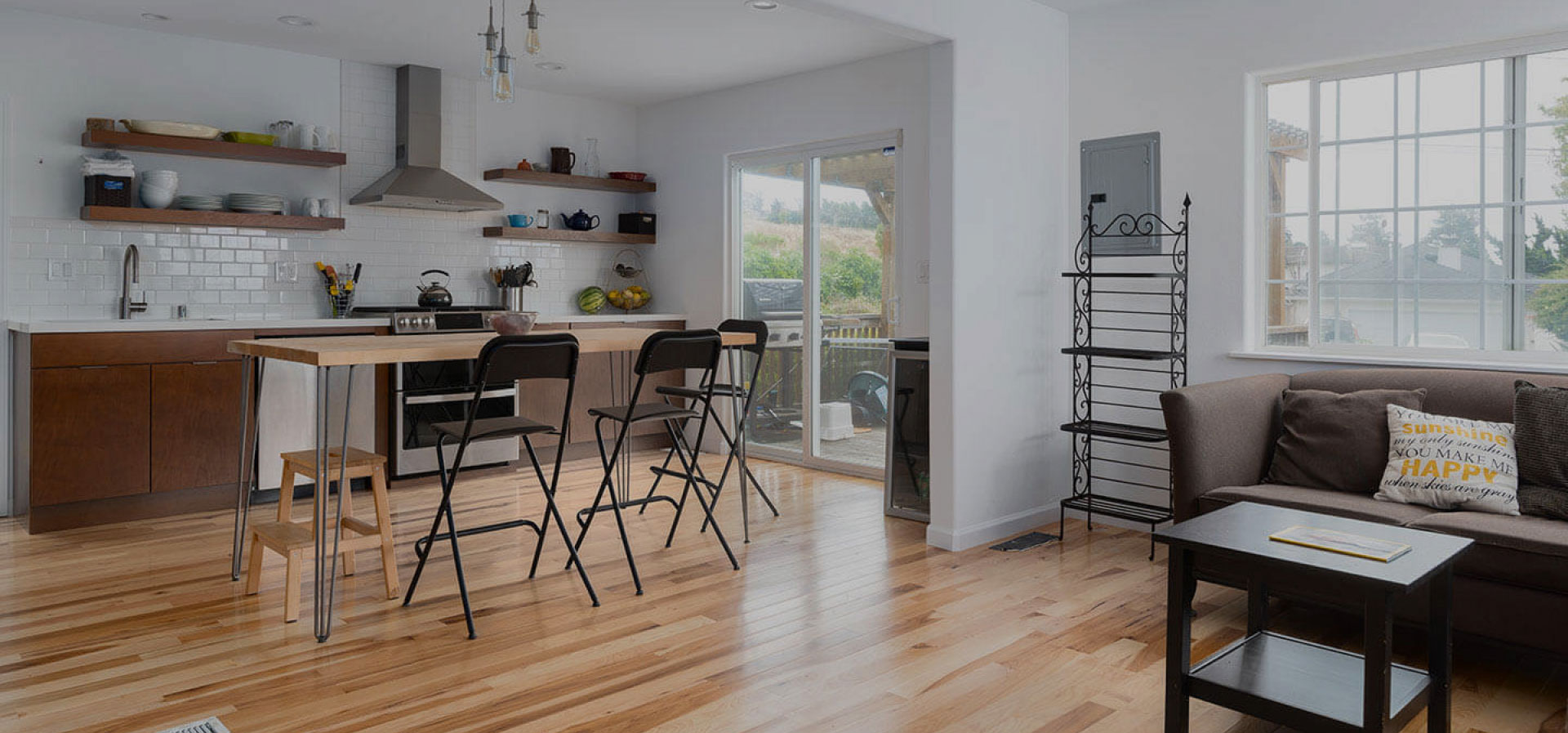 A modern kitchen with hardwood flooring, a center island, bar stools, and a dining table set for four, featuring a contemporary design with white cabinets and stainless steel appliances.