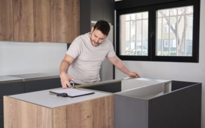 A man standing in a modern kitchen with stainless steel appliances, wooden cabinets, and a large island countertop.