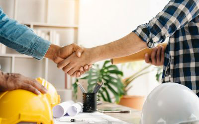 A group of people are shaking hands over a table with construction materials, indicating a professional agreement related to building or renovation projects.
