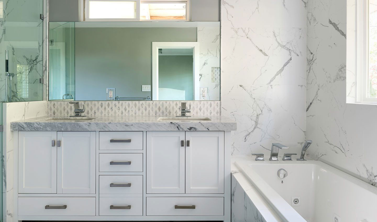 A modern bathroom with marble countertops, white cabinets, and a large mirror above the sink.