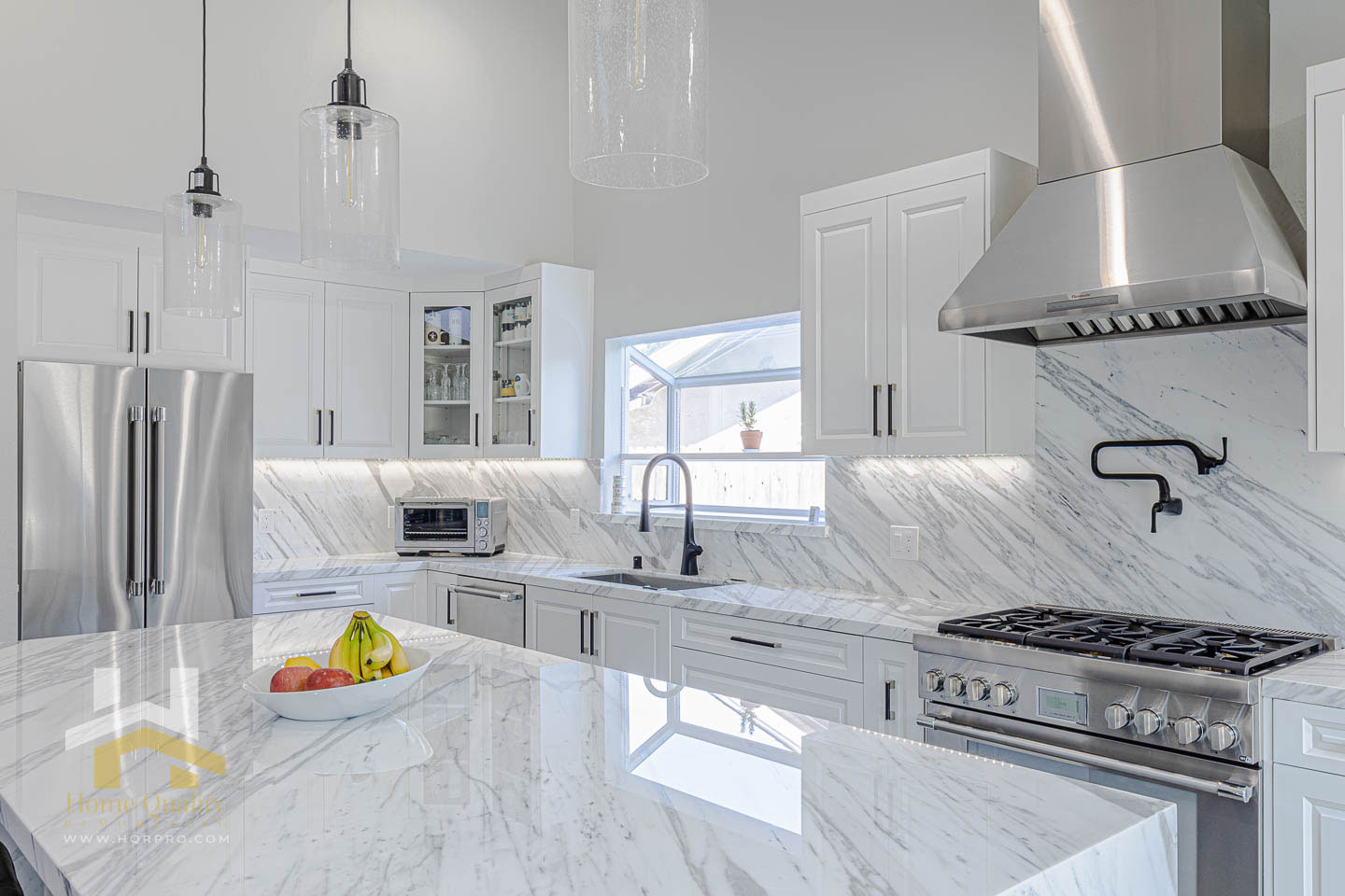 The image depicts a modern kitchen with a large island featuring a marble countertop, stainless steel appliances, and a metallic finish.